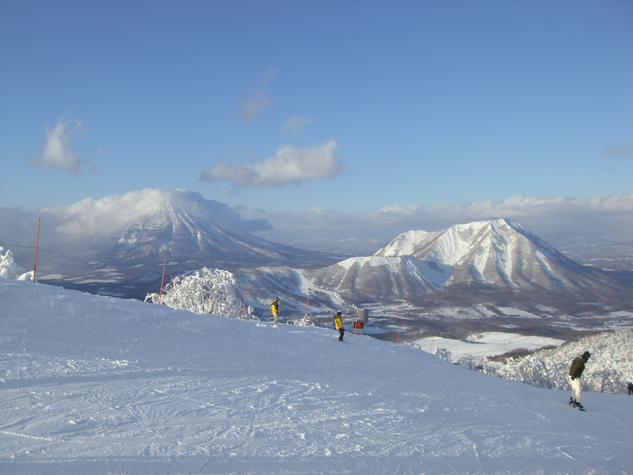 Skiers at Rusutsu with snowy Mount Shiribetsu and Mount Yotei beyond