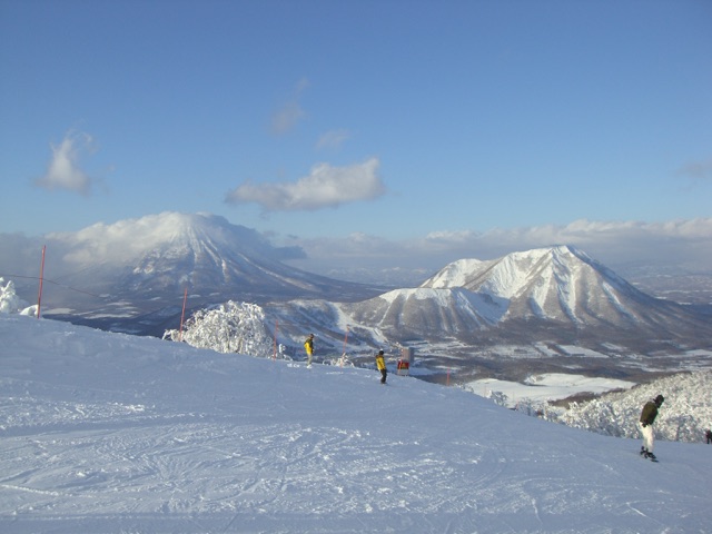 Skiers at Rusutsu with snowy Mount Shiribetsu and Mount Yotei beyond